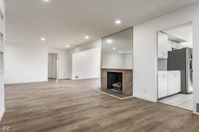 unfurnished living room featuring a fireplace, recessed lighting, a textured ceiling, light wood-type flooring, and baseboards