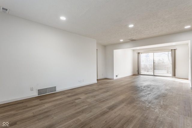 empty room featuring a textured ceiling, visible vents, and wood finished floors