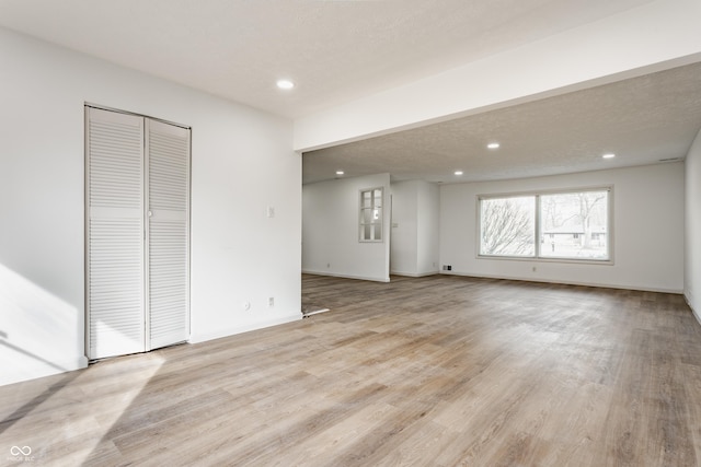 unfurnished living room featuring light wood-style floors, recessed lighting, a textured ceiling, and baseboards