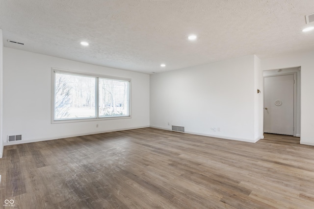 empty room with baseboards, a textured ceiling, visible vents, and wood finished floors