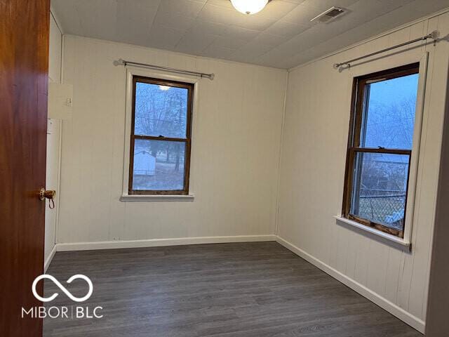 empty room featuring dark wood-style floors, visible vents, and baseboards