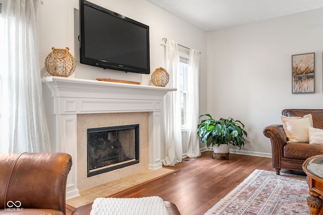 living room with a tile fireplace, baseboards, and wood finished floors