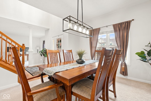 dining room featuring ornate columns, stairway, baseboards, and light colored carpet