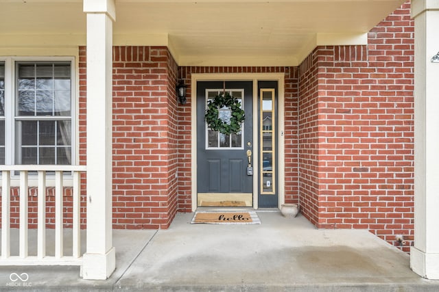 view of exterior entry with covered porch and brick siding