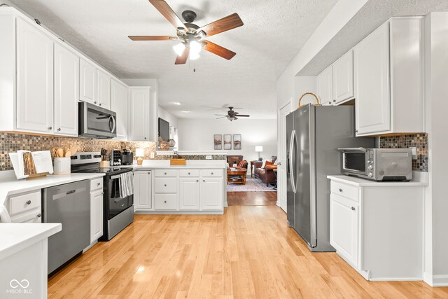 kitchen with light wood finished floors, stainless steel appliances, light countertops, white cabinetry, and a peninsula