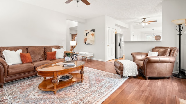 living area with light wood finished floors, a ceiling fan, baseboards, and a textured ceiling