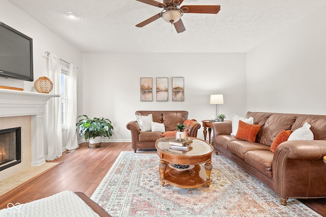 living area featuring a textured ceiling, ceiling fan, wood finished floors, and a tile fireplace