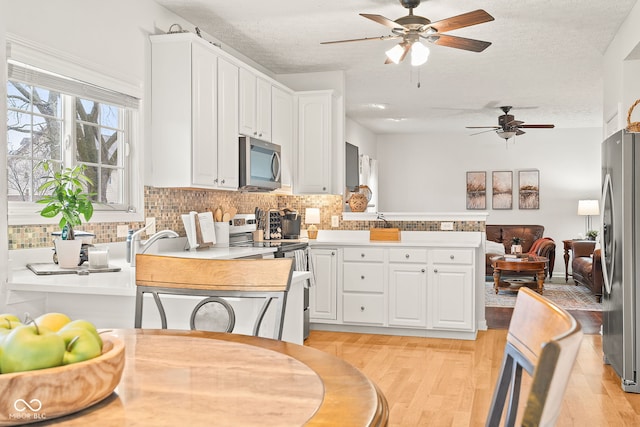 kitchen featuring stainless steel appliances, backsplash, light wood-style floors, white cabinets, and a peninsula