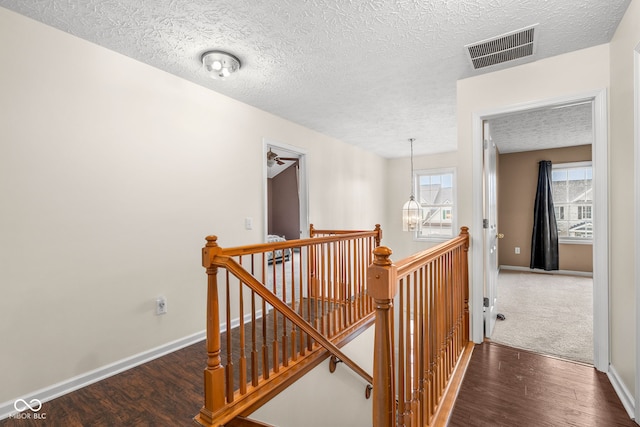 corridor with baseboards, visible vents, wood finished floors, and an upstairs landing