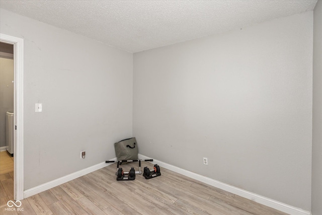 empty room featuring light wood-style flooring, baseboards, and a textured ceiling