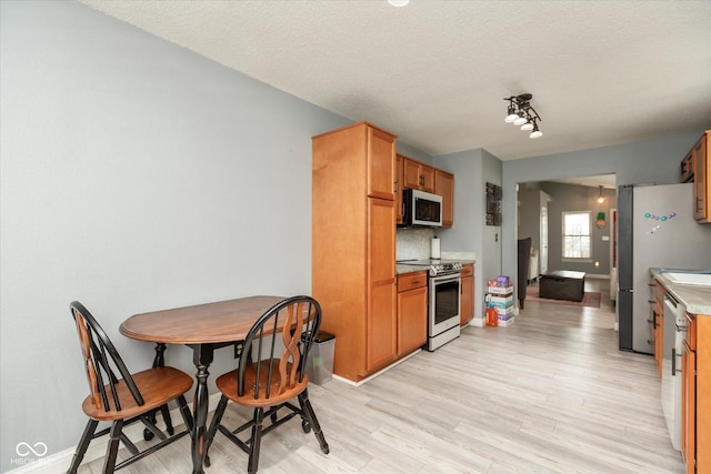 kitchen with stainless steel appliances, light countertops, a textured ceiling, light wood-type flooring, and baseboards