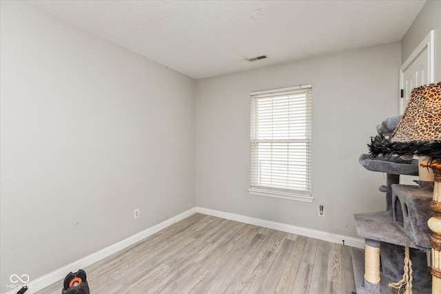 interior space featuring light wood-style floors, visible vents, baseboards, and a textured ceiling