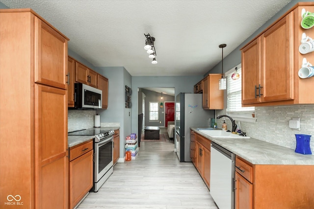 kitchen with a sink, light wood-style floors, light countertops, appliances with stainless steel finishes, and decorative backsplash