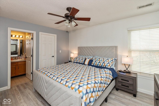 bedroom with a textured ceiling, ceiling fan, connected bathroom, visible vents, and light wood-type flooring