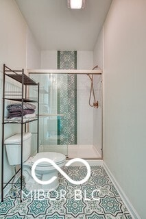 full bath with a stall shower, tile patterned floors, toilet, and baseboards