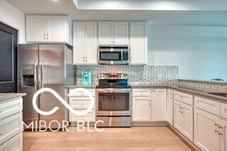 kitchen with white cabinets, light wood-style flooring, appliances with stainless steel finishes, and tasteful backsplash