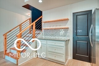 interior space with light wood-type flooring, stainless steel fridge, stairs, and backsplash