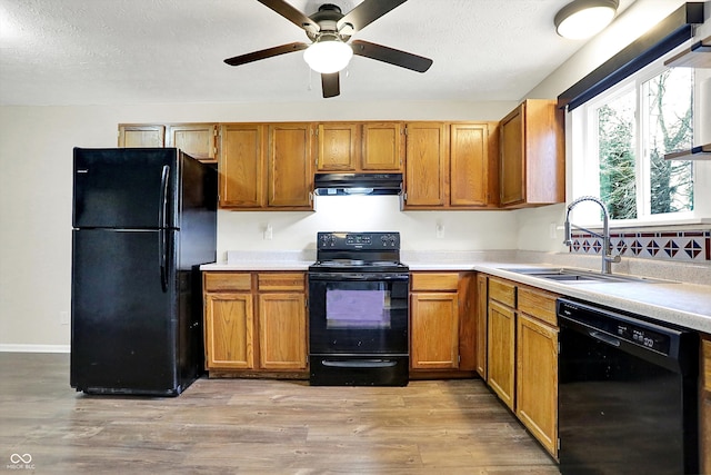 kitchen featuring a sink, light countertops, ventilation hood, light wood-type flooring, and black appliances