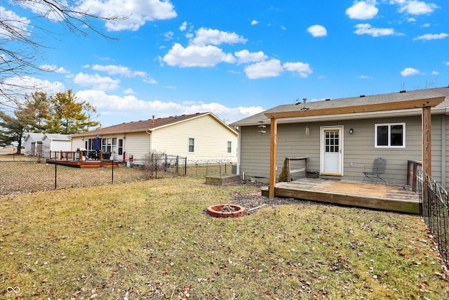 back of property with a fire pit, a fenced backyard, a lawn, and a deck