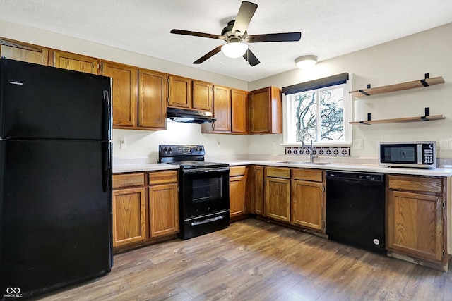 kitchen featuring brown cabinets, wood finished floors, under cabinet range hood, black appliances, and a sink