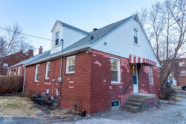 view of property exterior featuring roof with shingles and brick siding