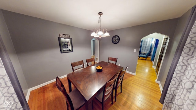 dining area with light wood-type flooring, an inviting chandelier, baseboards, and arched walkways