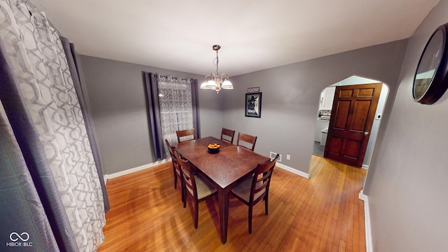 dining room featuring arched walkways, light wood finished floors, an inviting chandelier, and baseboards