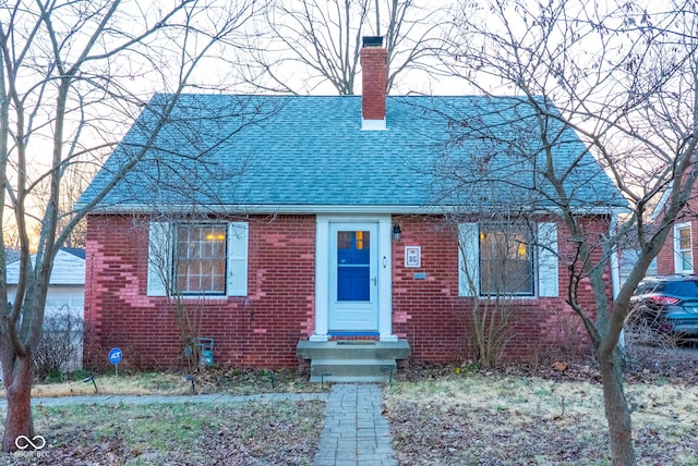 view of front of house featuring brick siding, a chimney, and a shingled roof