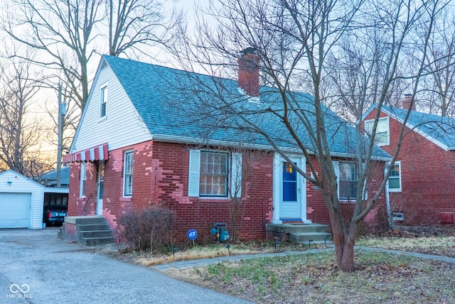 view of front of property with an outbuilding, brick siding, a shingled roof, a detached garage, and a chimney