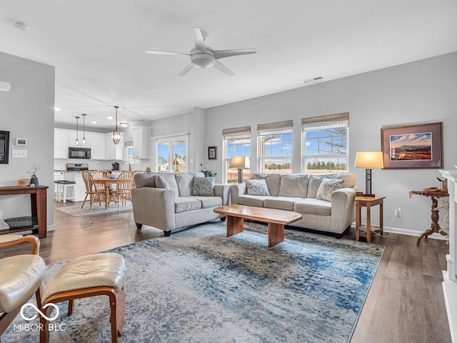 living area with baseboards, visible vents, a ceiling fan, and wood finished floors