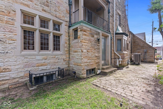 exterior space featuring entry steps, a balcony, central AC unit, and stone siding