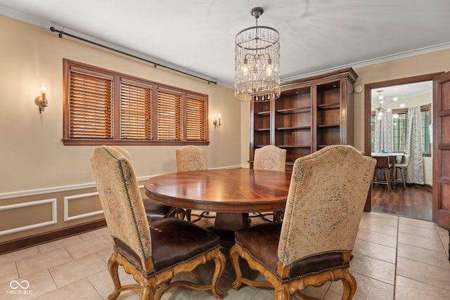 tiled dining space with a chandelier, a wainscoted wall, a decorative wall, and ornamental molding