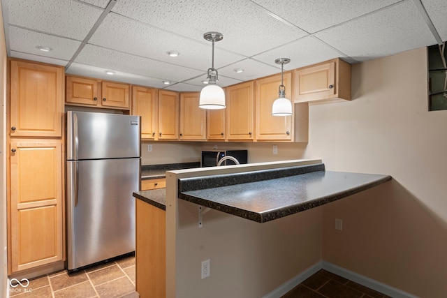 kitchen featuring a drop ceiling, dark countertops, appliances with stainless steel finishes, a peninsula, and hanging light fixtures