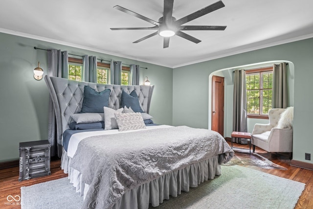 bedroom with wood finished floors, arched walkways, crown molding, baseboards, and ceiling fan