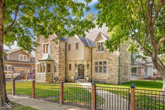 tudor house with a front lawn, stone siding, and a fenced front yard