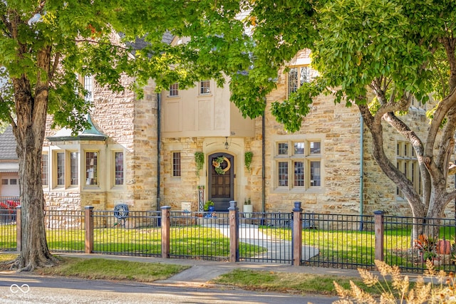 townhome / multi-family property with a front lawn, stone siding, and a fenced front yard