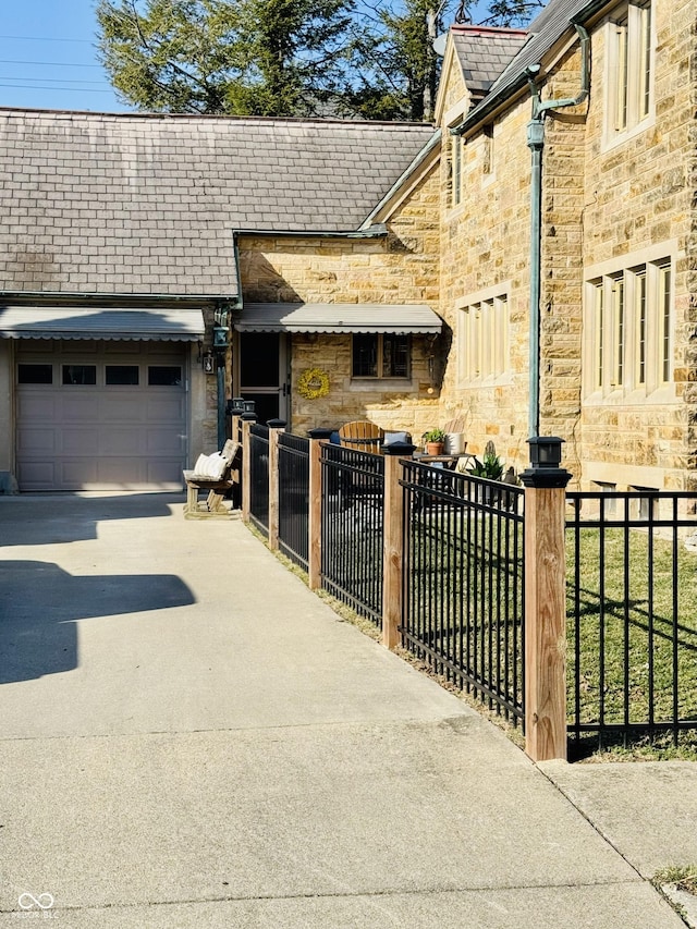 view of front of house featuring a fenced front yard, stone siding, concrete driveway, and a high end roof