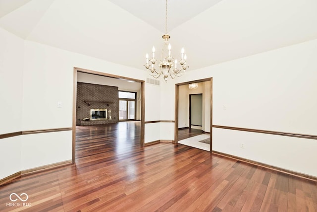 unfurnished dining area featuring lofted ceiling, visible vents, a brick fireplace, wood finished floors, and baseboards