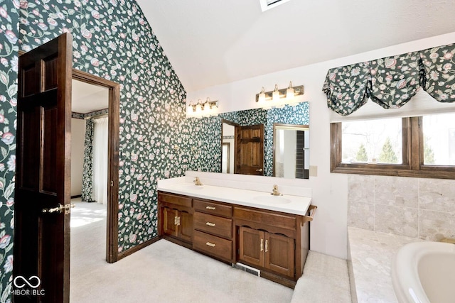 bathroom featuring double vanity, wallpapered walls, vaulted ceiling, a sink, and a bath