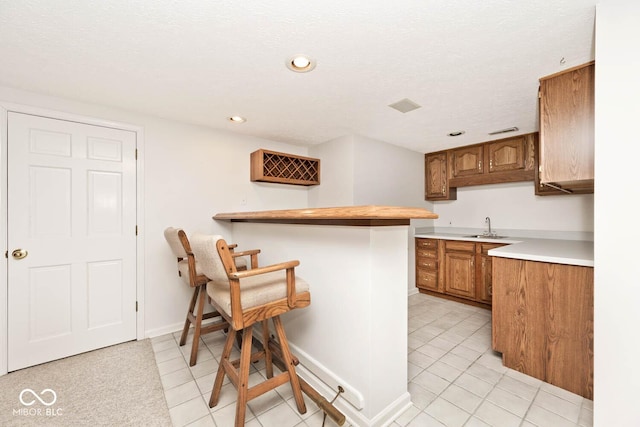 kitchen featuring brown cabinetry, a kitchen breakfast bar, a peninsula, light countertops, and a sink