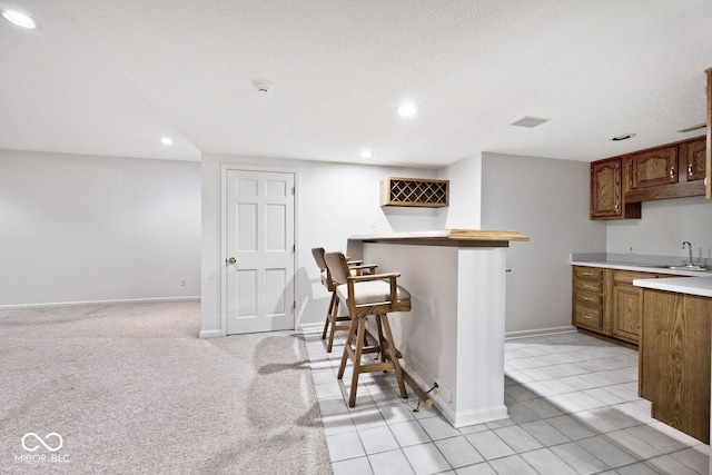 kitchen with brown cabinets, recessed lighting, light countertops, a sink, and baseboards