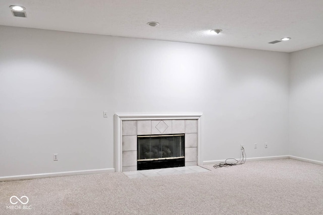 unfurnished living room with a textured ceiling, a tiled fireplace, carpet flooring, and baseboards