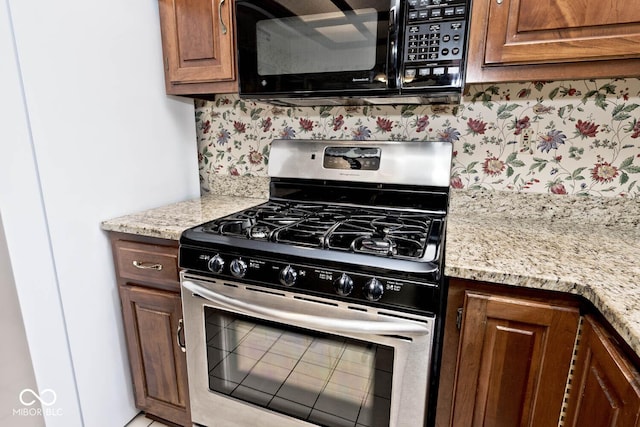 kitchen featuring tasteful backsplash, brown cabinetry, light stone counters, stainless steel gas range, and black microwave