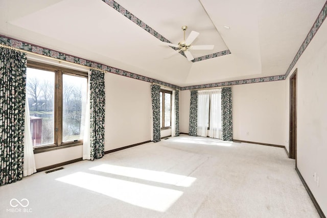 spare room featuring light colored carpet, a ceiling fan, baseboards, visible vents, and a raised ceiling