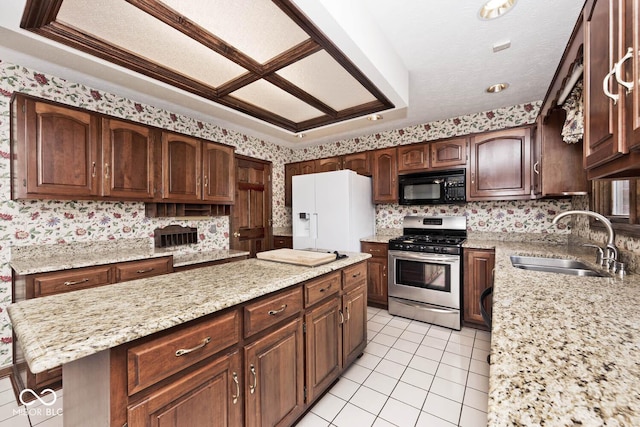 kitchen featuring gas range, a center island, white fridge with ice dispenser, black microwave, and a sink