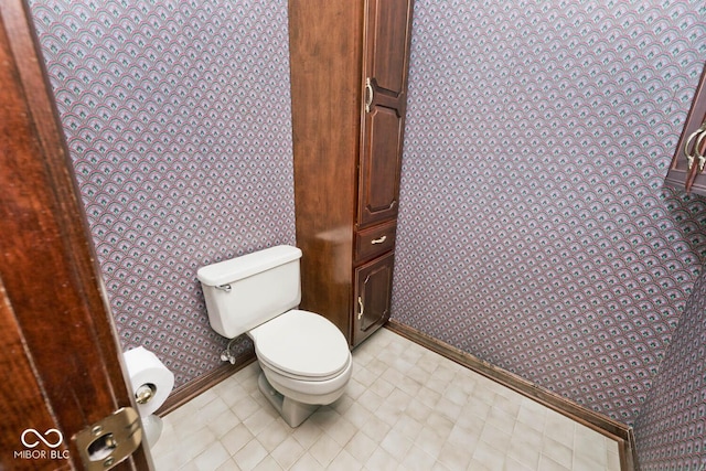 bathroom featuring toilet, wallpapered walls, and baseboards