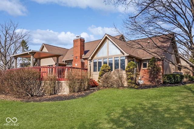 rear view of property with brick siding, a chimney, a lawn, a sunroom, and a deck