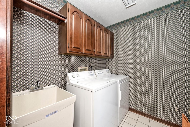 laundry room with light tile patterned floors, a textured ceiling, washing machine and dryer, a sink, and cabinet space