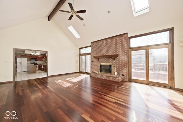 unfurnished living room featuring high vaulted ceiling, a skylight, a brick fireplace, and wood finished floors