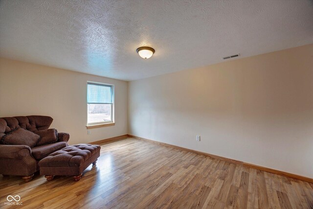 sitting room featuring light wood-type flooring, visible vents, baseboards, and a textured ceiling